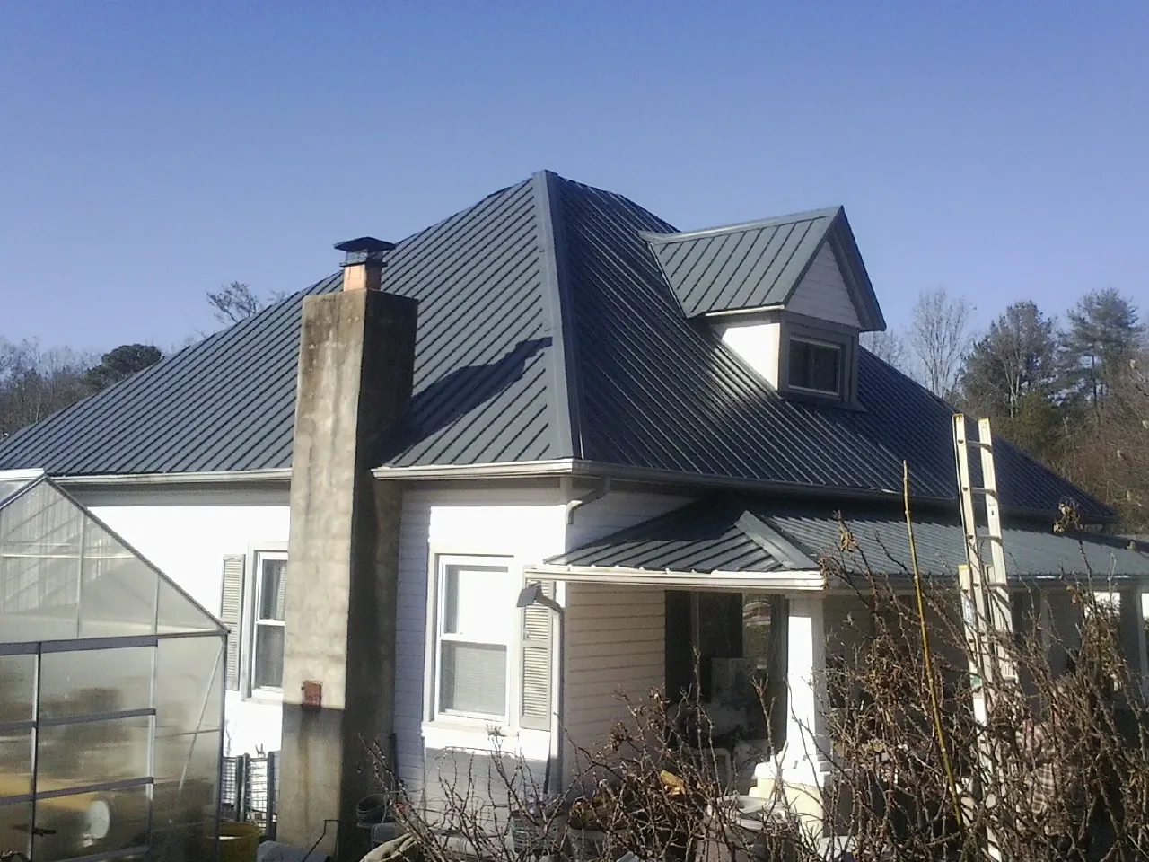 Dark blue standing seam metal roof on a white farmhouse with dormer — Slate & Tile Roof Repair by Roofing Brothers in Pleasant Plain
