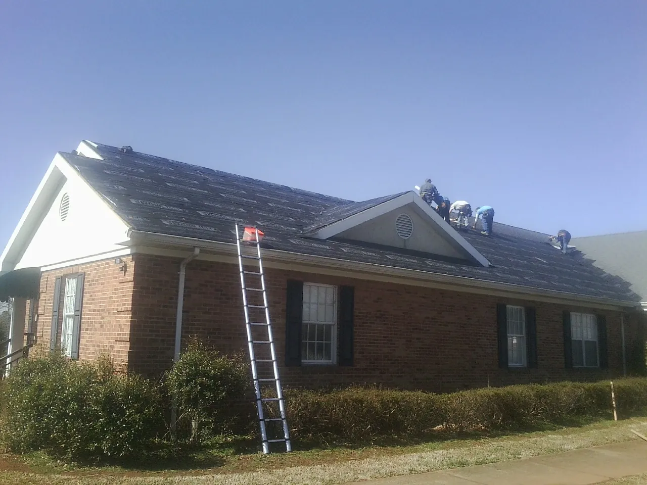Crew tearing shingles off a brick ranch roof with a ladder set — Emergency Roof Repair work by our crew in Pleasant Plain