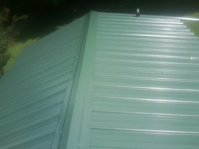New green metal panels meeting at the ridge of a roof — Flat Roof Repair work by our crew in Pleasant Plain