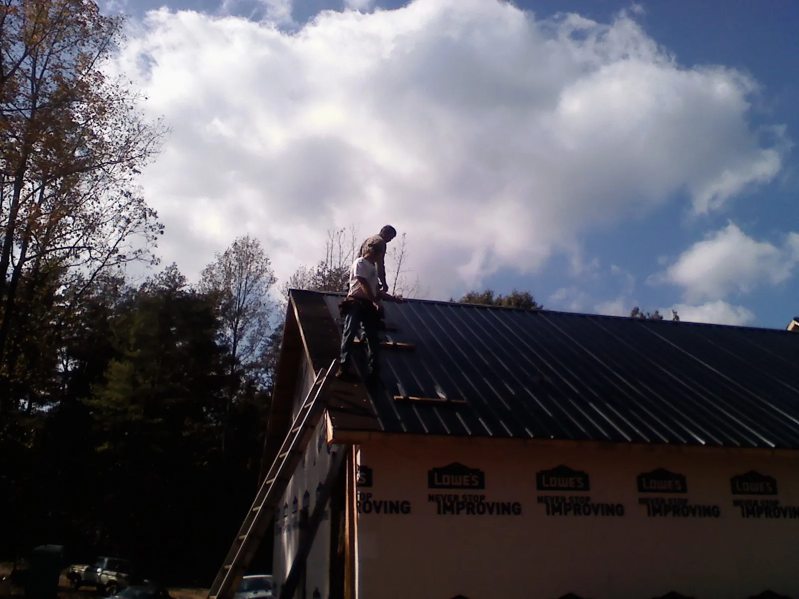 Roofer fastening dark metal panels high against a cloudy sky, from a Roof Inspection job in Pleasant Plain