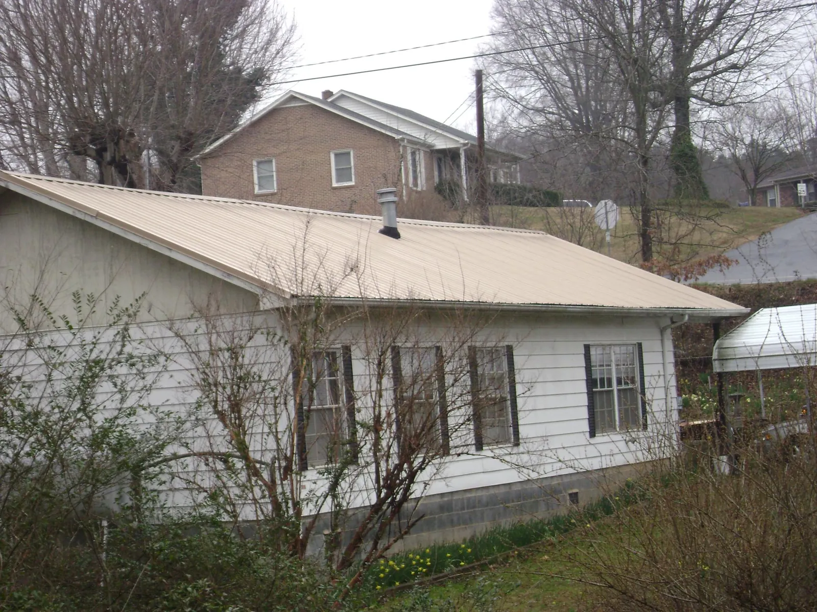 Tan metal roof on a white sided house set into a hillside — Commercial Roofing by Roofing Brothers in Pleasant Plain