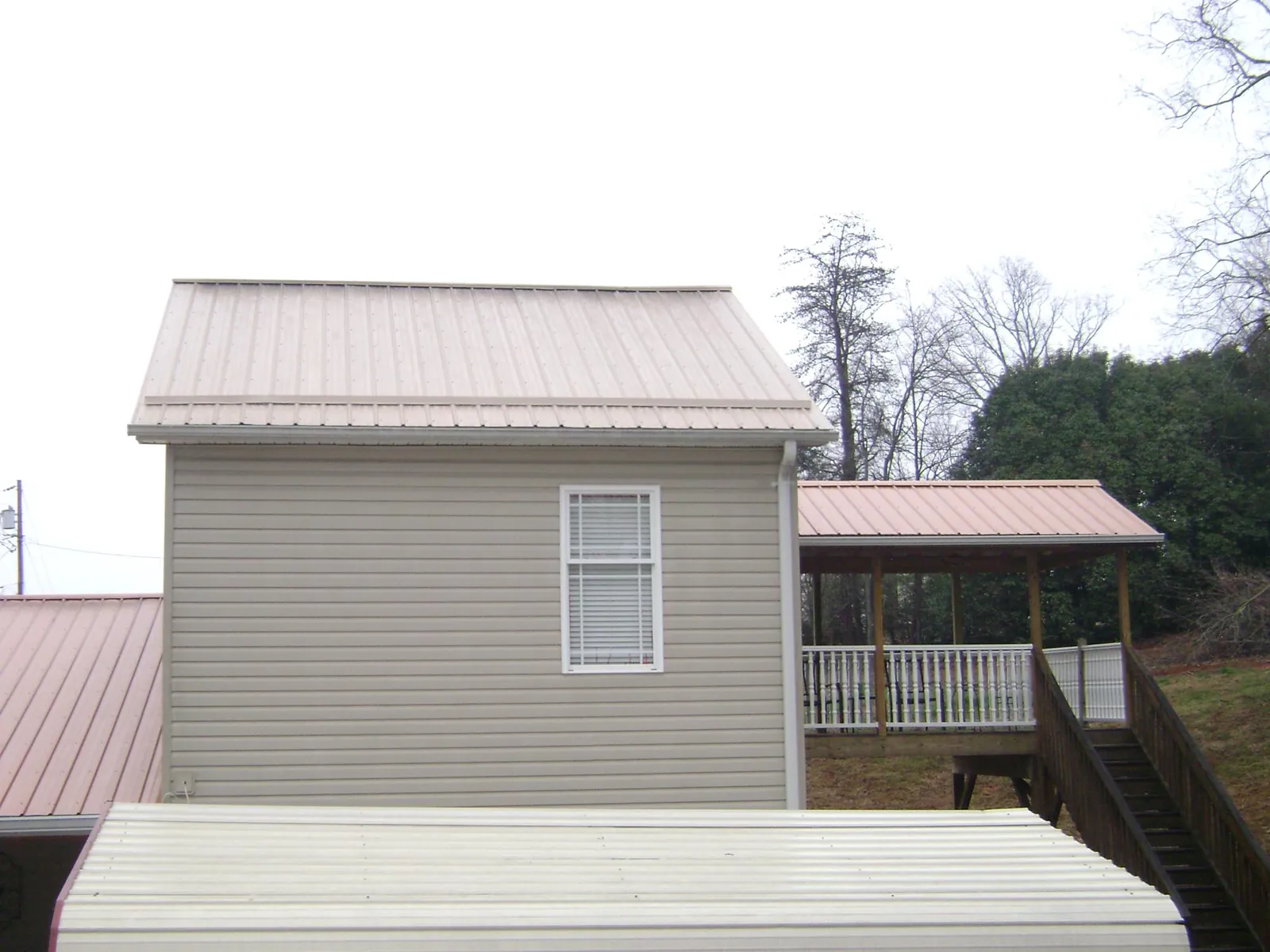 Tan metal roofs on a two story addition and attached porch, from a Roof Replacement job in Pleasant Plain